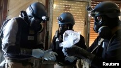 FILE - A U.N. chemical weapons expert, wearing a gas mask, holds a plastic bag containing samples from one of the sites of an alleged chemical weapons attack in Ain Tarma neighborhood of Damascus, Syria, Aug. 29, 2013.