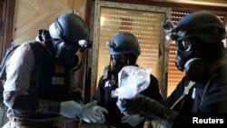 Para inspektur PBB dengan mengenakan masker gas membawa plastik yang berisi sampel yang diambil dari distrik Ain Tarma di pinggiran Damaskus, Suriah (29/8). 