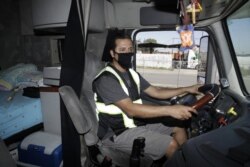 In this Monday, April 27, 2020, photo, truck driver Juan Giraldo poses for a photo inside his cab in Wilmington, California.