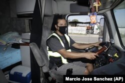 In this Monday, April 27, 2020, photo, truck driver Juan Giraldo poses for a photo inside his cab in Wilmington, California.