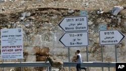 A Palestinian youth leads a donkey next to signs leading to Jewish settlements in the northern West Bank, 27 Sep 2010