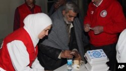 Nhân viên Hội Trăng lưỡi liềm Đỏ cung cấp thức ăn và nước cho một người đàn ông trước khi ông lên xe buýt rời khỏi thành phố Homs
