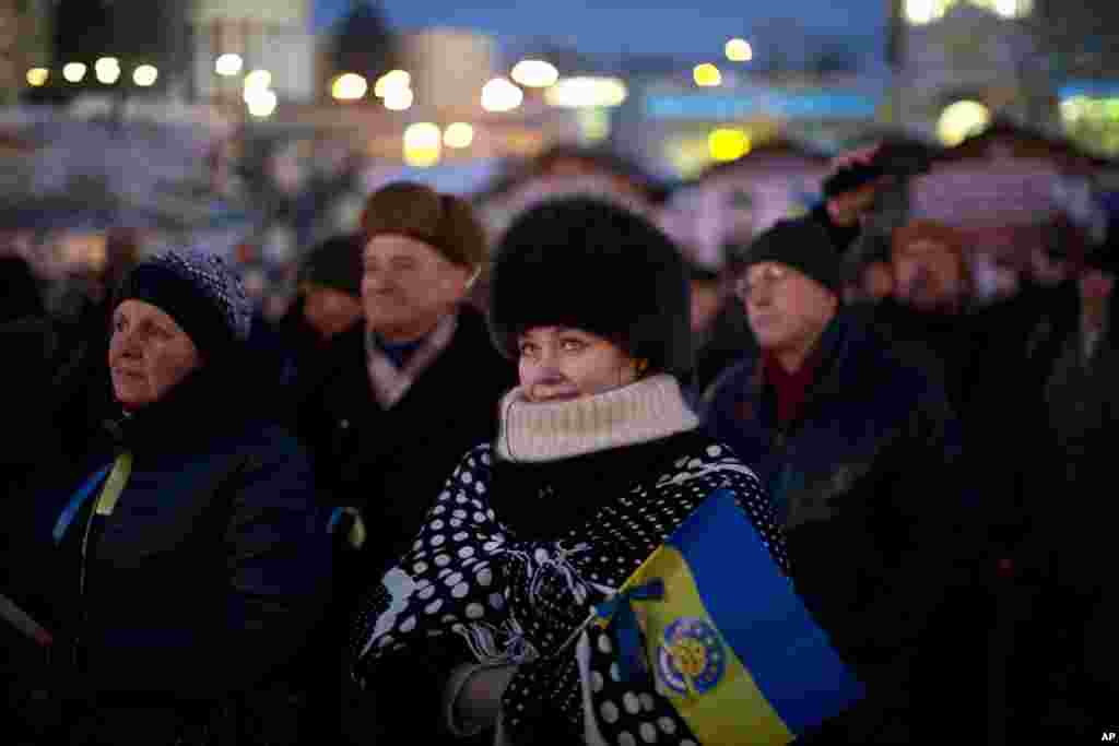 People, one with a Ukrainian flag, attend a political speech on a stage set in Kyiv&#39;s Independence Square, the epicenter of the country&#39;s current unrest. 