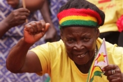 A woman celebrates while holding the Zimbabwean flag as Zimbabwean President Robert Mugabe arrives to mark 35 years of Independence at the National Sports stadium in Harare,