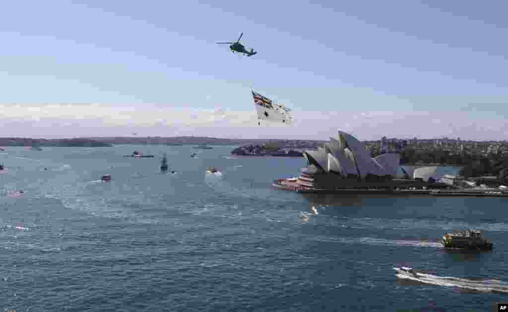 A Royal Australian Navy helicopter towing the Australian naval ensign passes over the Opera House during the International Fleet review, Sydney, Oct. 4, 2013.