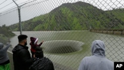 People stop to watch water flow into the iconic Glory Hole spillway at the Monticello Dam, Feb. 20, 2017, in Lake Berryessa, Calif. Water is flowing for the first time in over a decade into the 72-foot diameter hole due to the recent storms in California.