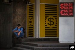 Seorang pria melihat ponselnya di sebelah tanda kantor pertukaran yang menunjukkan nilai tukar mata uang di Moskow, Rusia. (Foto: AP)