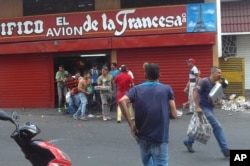 FILE - This photo provided by Heibort Barrios shows people running off with meat from a butcher shop in Turmero, Aragua state, near Maracay, Venezuela, June 28, 2017.