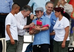 FILE - Colombia's President Juan Manuel Santos, second left, and the Revolutionary Armed Forces of Colombia, FARC, top commander Rodrigo Londono also known as Timoleon Jimenez or Timochenko, third left, greet the baby of a rebel couple during an act to commemorate the completion of the FARC disarmament process in Buenavista, Colombia, June, 27, 2017.