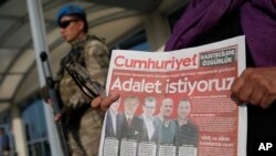 Under the watchful eye of a Turkish army soldier standing guard outside a court, a protester holds a copy of the Cumhuriyet newspaper, with headline in Turkish reading: 'We want justice," during a demonstration against the trial of journalists and staff from the newspaper, accused of aiding terror organizations, in Silivri, Turkey, Sept. 11, 2017.
