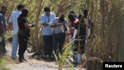 A woman identifies the bodies of her relatives, a father and son, as police investigators and forensic technicians process the crime scene, in San Luis Talpa, El Salvador, Feb. 26, 2016.