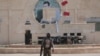 A Kurdish fighter from the People's Protection Units (YPG) carries his weapon as he walks at the faculty of economics where a defaced picture of Syrian President Bashar al-Assad is seen in the background, in the Ghwairan neighborhood of Hasaka, Syria, Aug. 22, 2016.