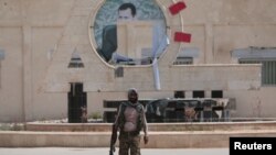 A Kurdish fighter from the People's Protection Units (YPG) carries his weapon as he walks at the faculty of economics where a defaced picture of Syrian President Bashar al-Assad is seen in the background, in the Ghwairan neighborhood of Hasaka, Syria, Aug. 22, 2016.