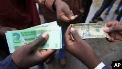 FILE: Zimbabweans compare the new note with the U.S. dollar note following the introduction of new notes by the Reserve Bank of Zimbabwe in Harare, Nov, 28, 2016.
