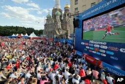 FILE - People watch on a huge screen the 2018 soccer World Cup match between Russia and Saudi Arabia at a fan zone in St. Petersburg, Russia, June 14, 2018.