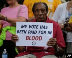 FILE - A man holds a protest sign at rally in Winston-Salem, North Carolina, after the start of a federal trial challenging the state’s voting rights law, July 13, 2015.