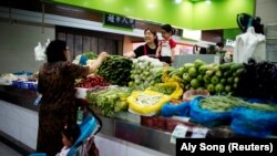 FILE PHOTO: Two grandmothers with their granddaughter trade vegetables at a market on the outskirts of Shanghai, China June 3, 2021