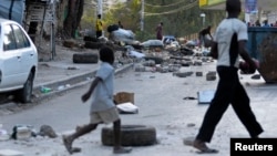 FILE - People walk through a litter-filled street after residents of a camp for people displaced by Haiti's Jan. 2010 earthquake blocked streets after some tents were destroyed, Port-au-Prince, Feb. 15, 2013. 