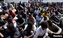 ຊາວອົບພະຍົບອາຟຣິກາ ທີ່ເຂົ້າເມືອງຜິດກົດໝາຍ ນັ່ງຢູ່ລະຫວ່າງການຢ້ຽ,ຢ້າມຂອງເຈົ້າໜ໊າທີ່ ອງົການສະຫະປະຊາຊາດ ທ່ີນະຄອນ ຕຣິໂປລີ ປະເທດອີຕາລີ.