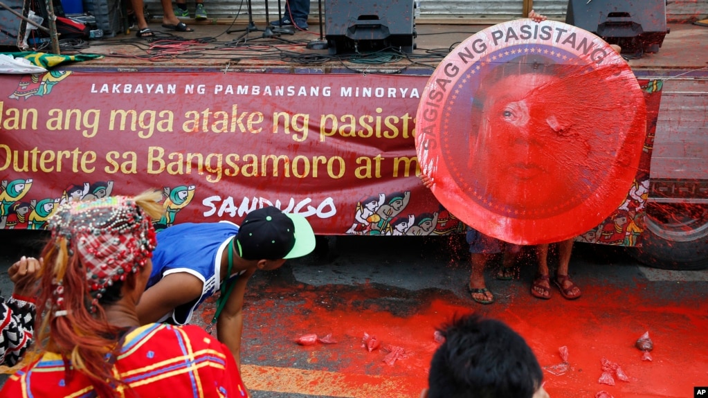 Indigenous people, including Muslims from the besiege city of Marawi, throw red paint at the mock seal of President Rodrigo Duterte to protest the continued siege and the martial law imposed by Duterte on the Mindanao region, Aug. 31, 2017, in Manila, Philippines.