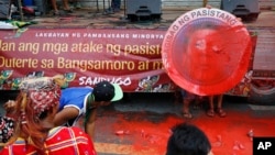 Indigenous people, including Muslims from the besiege city of Marawi, throw red paint at the mock seal of President Rodrigo Duterte to protest the continued siege and the martial law imposed by Duterte on the Mindanao region, Aug. 31, 2017, in Manila, Philippines.