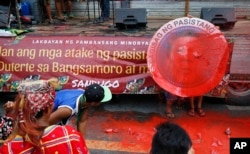Indigenous people, including Muslims from the besiege city of Marawi, throw red paint at the mock seal of President Rodrigo Duterte to protest the continued siege and the martial law imposed by Duterte on the Mindanao region, Aug. 31, 2017, in Manila, Phi
