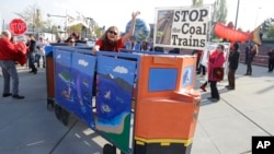 Seorang pemrotes menaiki kereta batubara tiruan saat para pengunjuk rasa lainnya melakukan aksi protes menentang beroperasinya kereta pembawa batubara untuk tujuan ekspor melewati negara bagian Washington di Tacoma, Washington DC. (Foto: dok).
