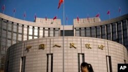 FILE - In this March 10, 2017, file photo, a woman walks past the headquarters of the People's Bank of China in Beijing. China’s central bank is planning to issue digital currency with tracking controls it will supervise.