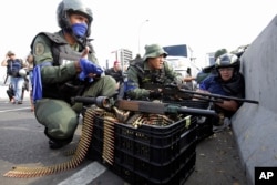 An anti-government protester, right, takes cover amid rebel troops who are rising up against the government of Venezuela's President Nicolas Maduro, on an overpass outside La Carlota military airbase as they confront loyal troops at the base.