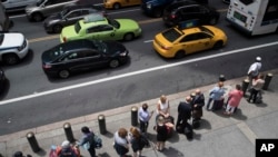 FILE - A ride-hailing car, a yellow cab and a green cab make their way across 42nd Street as passengers wait in line at a taxi stand outside Grand Central Terminal in New York, Aug. 1, 2018.