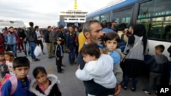A Syrian man holds his two children as the other two family members follow him after their arrival from the Greek island of Lesbos at the Athens' port of Piraeus, Wednesday, Sept. 30, 2015.