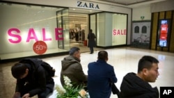 2018年1月12日，在北京一家购物中心的Zara商店外，购物者们看着他们的智能手机。