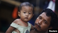 A migrant worker from Burma holds his daughter in front of their house in the port town of Mahachai, near Bangkok, September 24, 2011. 