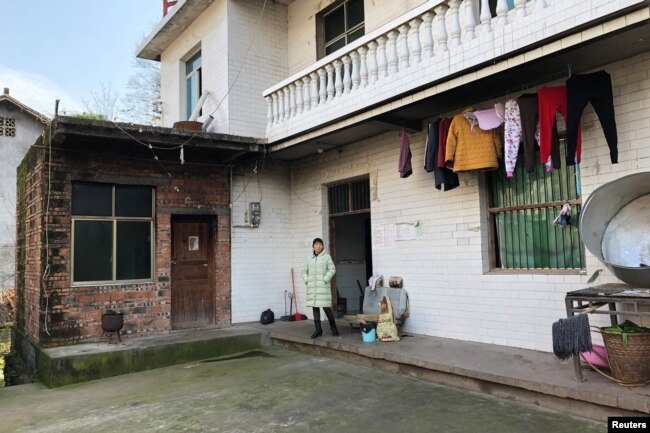 FILE - The wife of silicosis patient Wang Zhaohong stands in front of their house in Sangzhi county, Hunan province, China, Nov. 27, 2018.