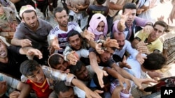 FILE - Displaced Iraqis from the Yazidi community gather for humanitarian aid at the Syria-Iraq border at Feeshkhabour border point, northern Iraq, Aug. 10, 2014.