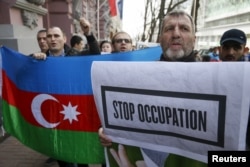 FILE - People hold up an Azerbaijani national flag and a sign during a rally in support of Azerbaijan over the conflict in the breakaway Nagorno-Karabakh region, outside the Armenian embassy in Kiev, Ukraine, April 8, 2016.