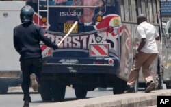 A riot policeman and an officer in plain clothes chase demonstrators who got into a bus near the IEBC, Independent Electoral and Boundaries Commission offices, in Nairobi, Kenya, Oct. 6, 2017.