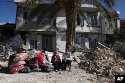 Survivors sit in front of a destroyed house on the earthquake site in Sarpol-e-Zahab in western Iran, Nov. 14, 2017.