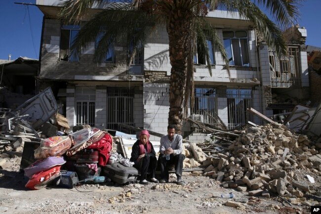 Survivors sit in front of a destroyed house on the earthquake site in Sarpol-e-Zahab in western Iran, Nov. 14, 2017.