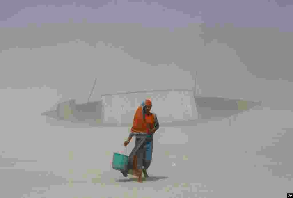 An Indian woman carries a bucket filled with drinking water as she walks on dry mud against blowing sand, along the Brahmaputra River on the eve of World Water Day in Gauhati. World Water Day is observed annually on Mar. 22 to recognize the global need to save, conserve and manage water resources for future generations. 