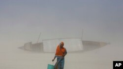 Seorang perempuan India membawa satu ember berisi air minum ketika berjalan di lumpur kering di tengah tiupan pasir, sepanjang sungai Brahmaputra di malam Hari Air Sedunia di Gauhati, India, 21 Maret 2014. (Foto: dok.)