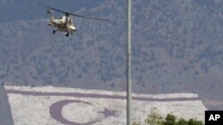 FILE - A Russian made military helicopter of Cypriot air forces flies over the military parade as a giant painting of Turkish Cypriot breakaway flag is seen on Pentadaktilos mountain at the north part in capital Nicosia in the divided island of Cyprus.