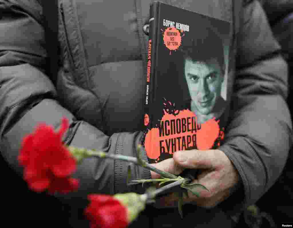A visitor holds flowers and a book "Confessions of the Rebel" by Russian leading opposition figure Boris Nemtsov while waiting to attend a memorial service before the funeral of Nemtsov in Moscow, March 3, 2015.
