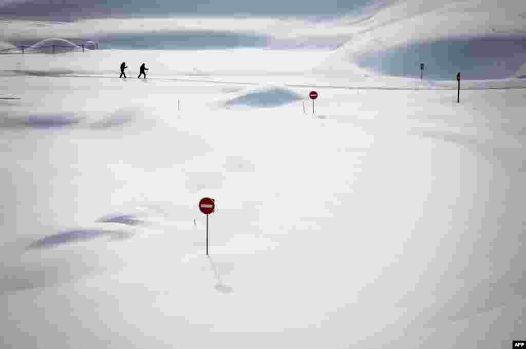 Two skiers pass by traffic signs covered in the snow by the Dappes Car Park near La Dole, Switzerland, Jan. 26, 2021.