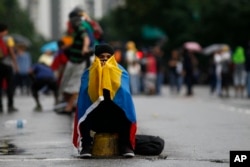 FILE - A masked anti-government protester, with a Venezuelan national flag wrapped around him, sits on the edge of a median strip in Caracas, Venezuela, June 28, 2017.