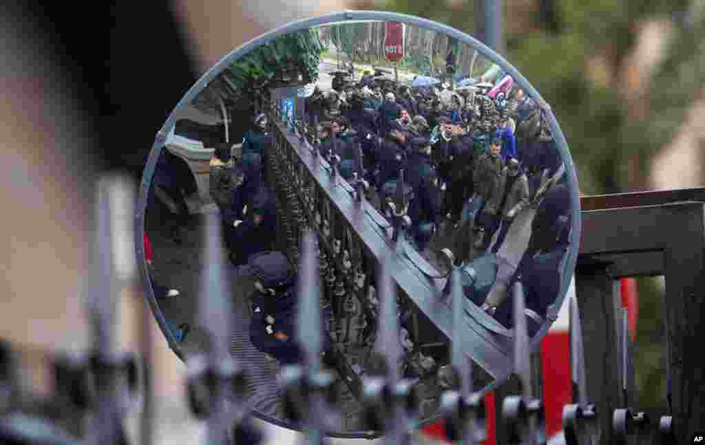 Police, seen reflected in a street mirror, guard the entrance of a polytechnic as students gather to protest education cuts and lay-offs of professors in Madrid, Spain. 