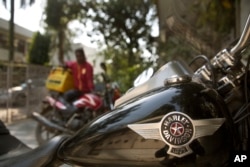 FILE - A delivery boy sits on his Indian motorcycle and looks at a Harley-Davidson Fat Boy motorcycle parked in a residential area in New Delhi, India, March 1, 2017.