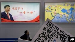 An attendee at a conference looks up near a portrait of Chinese President Xi Jinping with the words "Xi Jinping and One Belt One Road" and "One Belt One Road Strategy," in Beijing, April 28, 2017.