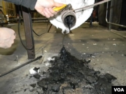 Many different types of unwashed plastic waste are melted together in a combustion chamber. Here, John Bordynuik, CEO of JBI, Inc., pulls a sample to determine what kind of fuel he wants to produce. (VOA/D. Robison)