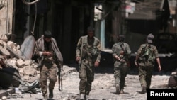 FILE - Syria Democratic Forces (SDF) fighters walk on the rubble of damaged shops and buildings in the city of Manbij, in Aleppo Governorate, Syria, Aug. 10, 2016.